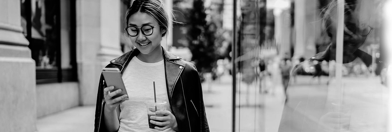 Young girl around town looking at smart phone with glasses and holding an iced coffee.